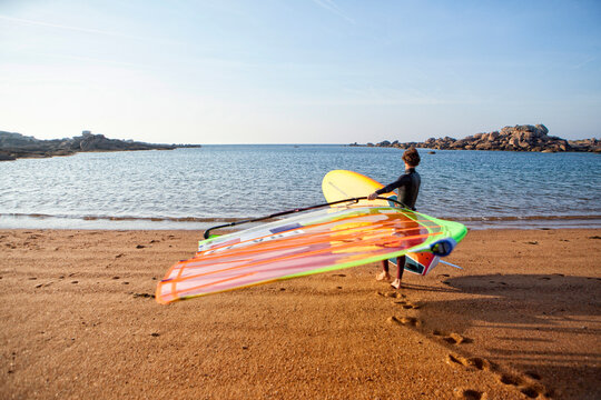 Pierre Le Coq carrying his windsurf heading for a training session on the "Cote de Granit Rose" ( Pink Granite Coast ), Tr&Atilde;&copy;gastel, Brittany, France.