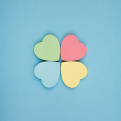 Fototapeta na wymiar Collection of different heart pastel-colored sheets of note papers ready for your message in shape of four-leaf clover on blue background. Top view. Close up. Sticky notes.