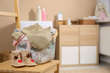 Fototapeta na wymiar Laundry basket with baby clothes and shoes on wooden chair indoors, space for text