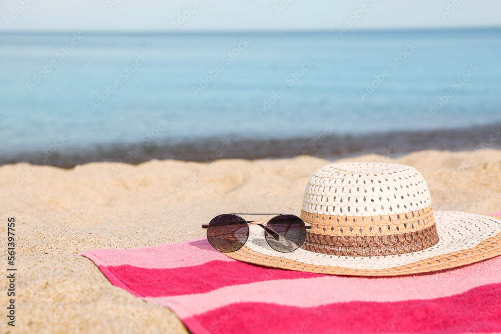 Wall mural Beach towel with straw hat and sunglasses on sand near sea. Space for text