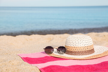 Beach towel with straw hat and sunglasses on sand near sea. Space for text