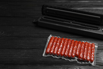 Vacuum packing sealer and plastic bag of sausages on black wooden table, space for text