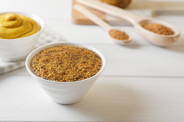 Bowls of whole grain mustard on white wooden table. Space for text