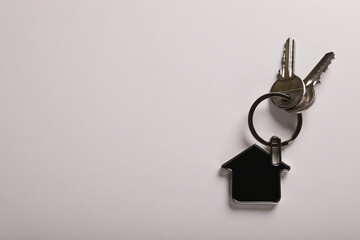 Keys with trinket in shape of house on white background, top view and space for text. Real estate agent services