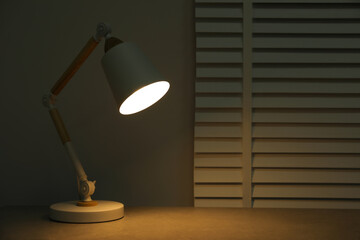 Stylish modern desk lamp on table at night, space for text