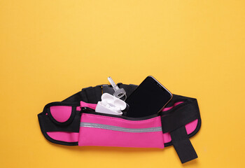 Stylish pink waist bag with smartphone, key and earphones on orange background, flat lay. Space for...