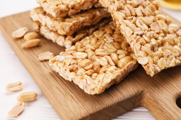 Board with tasty kozinaki bars, peanuts and honey on white wooden table, closeup