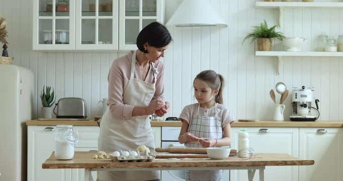 Loving older grandmother and little cute granddaughter cooking together in kitchen, making homemade pastries from fresh natural farm products. Teach, share skills with kid, family pastime and cookery