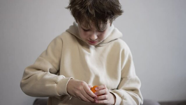 Boy of twelve years old in beige hoodie peels a tangerine. Kid wants to have a bite of a fruit.