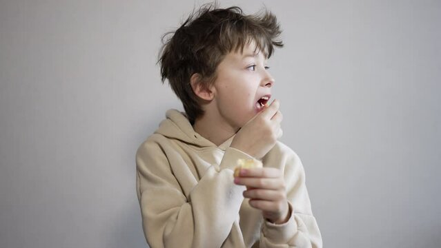 Calm brunet teenager eating a tangerine. Boy with messy hair eats fruit looking around and then into camera.