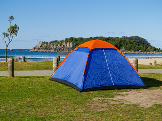 Small blue and orange tent on lawn beside beach