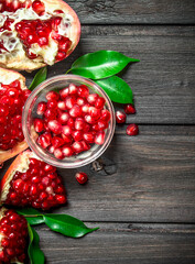 Pomegranate seeds in a bowl and pieces of ripe pomegranate with leaves.