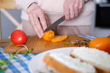 Aged woman cuts fresh vegetables for healthy sandwiches