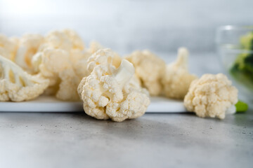 Cauliflower florets close-up on cutting board on a light grey stone background