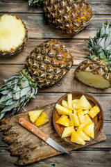 Fototapeta premium Sliced pineapple in a bowl on a cutting Board with a knife and a whole pineapple.