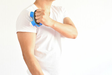 Hombre latino usando un masajeador portatil para aliviar dolor en el hombro.