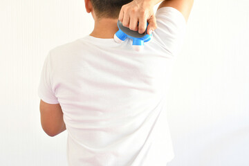 Hombre latino usando un masajeador pequeño para tratar dolor en la espalda. - obrazy, fototapety, plakaty