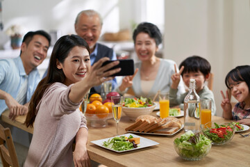 multi generational asian family taking a selfie at dining table