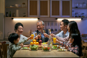 three generation asian family toasting while having dinner together