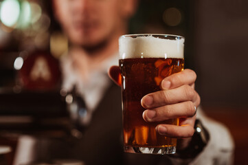 bartender's hand with a glass of light draft beer with foam in bar close-up