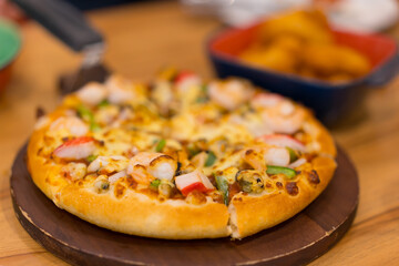 scooping seafood pizza dough thick and soft cheese with shrimp mussels squid and crab sticks on wooden tray table with nuggets in bowl for iodine cuisine to family eating at italian food restaurant