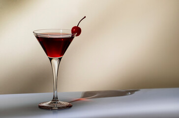 Black Manhattan cocktail with whiskey and red vermouth garnished with maraschino cocktail cherry in martini glass. Beige background, hard light