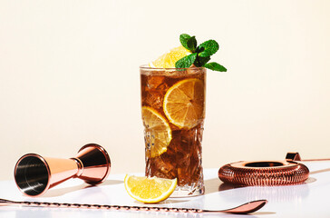 Long Island ice tea cocktail with vodka, rum, tequila, gin, liquor, lemon juice, cola and ice, garnished with lemon slice and mint in highball glass. Beige background, hard light - obrazy, fototapety, plakaty
