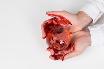 A woman holds a crystal globe smeared in blood on a white background.