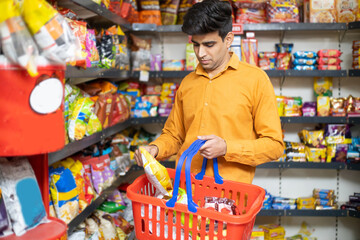 Young Indian man buying grocery at shop or supermarket. Asian male choose snacks and food items...