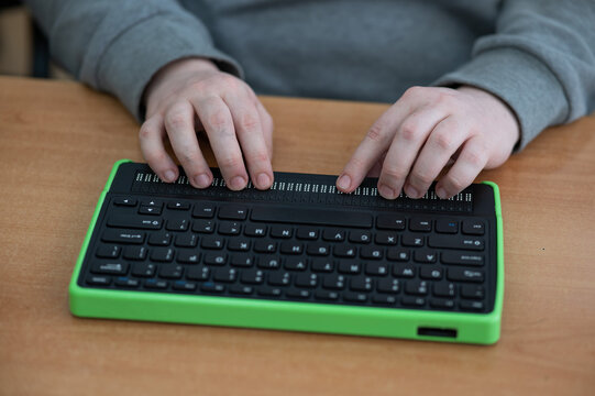 A blind man uses a computer with a Braille display and a computer keyboard. Inclusive device.
