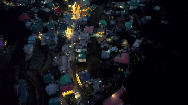 pan up aerial drone reveal shot going from lights of manali hill station town to fog covered mountains himalaya lit by dawn dusk light showing tourist hub in Himachal India
