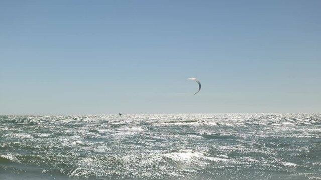 Wind Surfer rides waves far away on clear blue sky 
day in Slow Motion Grange Beach South Australia