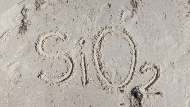 SiO2 Silicon Dioxide Silica written on beach in sand
with finger Height Zoom Up in Slow Motion