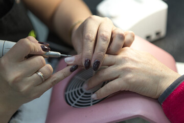 Obraz na płótnie Canvas Manicure process in spa salon, close-up. A manicurist files a client's nails at a table. Removal of the nail plate with a cutter. Shallow depth of field