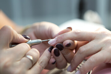 Manicure process in spa salon, close-up. A manicurist files a client's nails at a table. Removal of the nail plate with a cutter. Shallow depth of field