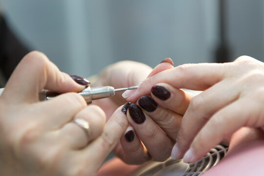 Manicure process in spa salon, close-up. A manicurist files a client's nails at a table. Removal of the nail plate with a cutter. Shallow depth of field