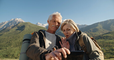Old couple having a hike in spring mountains, then stopping to take a picture on a smartphone. Senior caucasian family spending time together travelling after retirement - tourism concept 