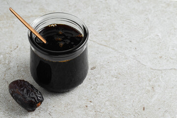 Date syrup in a glass jar, spoon, whole date fruit. Close up. Beige background with stone texture....