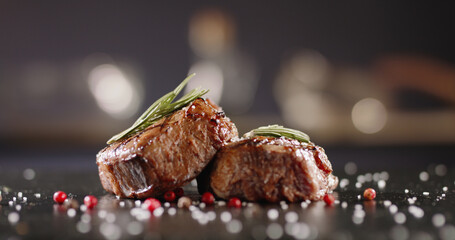 Two Pieces of red meat steak with rosemary served on black stone surface. Blur kitchen on...
