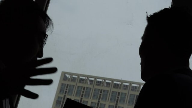 Silhouettes of people talking and plotting in front of a company window