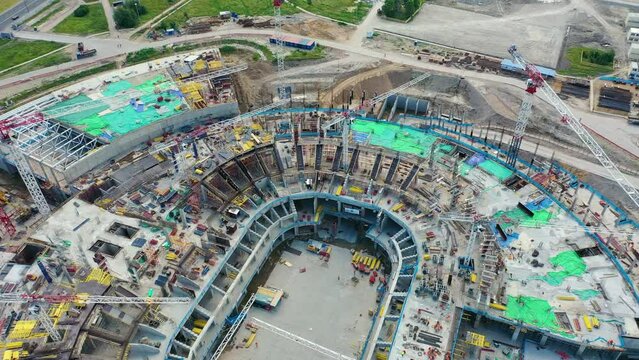 Building site of the arena stadium, a lot of construction equipment at work aerial top view