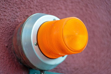 Orange saftey light on side of red building with stucco exterior and gray metal housing for bulb in an industrial area