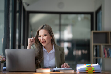 The cheerful business lady working on a laptop in the office, an Asian happy beautiful businesswoman in a formal suit working in the workplace. Attractive female employee office worker smile.