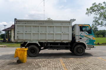 Logistics box truck is parked in city park near a yellow trash bin