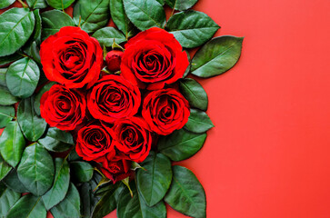 Red roses with leaves set as love shape on red background for Valentines day concept.