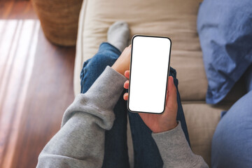 Top view mockup image of a woman holding mobile phone with blank desktop white screen while lying...