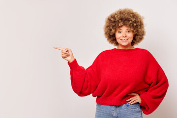 Positive woman plus size, smiles cheerfully and pointing finger a side, happy charming female dressed in red sweater