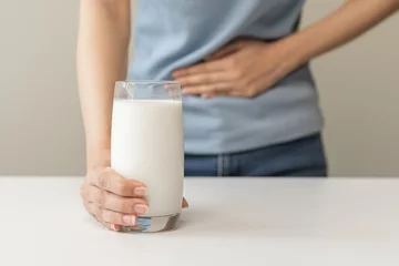 Fotobehang Pain, suffering asian young woman having a stomachache, abdominal pain or digestive, hand in holding belly after drink glass of milk. Lactose intolerance, allergy from dairy food, health care problem. © KMPZZZ