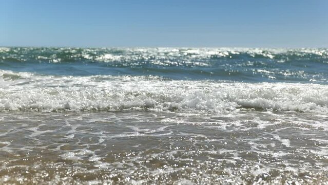 Small Waves clean and blue roll into shallow 
shore in slow motion under Blue Sky Grange Beach South Australia