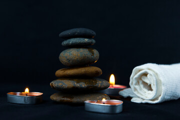 Peace of dark stones on dark background, layers of hot stones use for massage setting lit by candles light and  Massage therapy for wallper, pattern, poster and banner design..